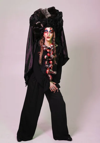 Moda, belleza, gente y concepto de Halloween: Mujer joven con un maquillaje creativo brillante y un gran tocado negro . — Foto de Stock
