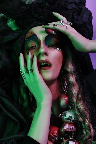 Mode, Schönheit, Menschen und Halloween-Konzept: junge Frau mit grellem, kreativem Make-up und großer schwarzer Kopfbedeckung. — Stockfoto
