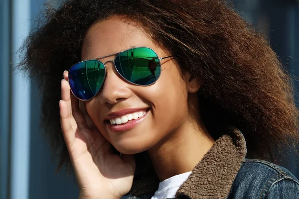 Ładna kobieta w okularach przeciwsłonecznych z doskonałymi zębami i ciemną, czystą skórą odpoczywającą na świeżym powietrzu, uśmiechnięta po otrzymaniu pozytywnych wieści. — Zdjęcie stockowe