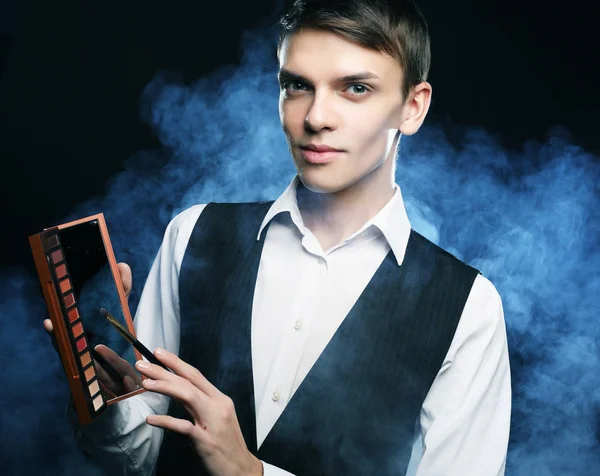 Professional makeup artist posing in studio, holds a palette of shadows.Against the background of smoke. — Stock Photo, Image