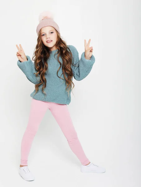 Bambina con cappello rosa e maglione blu che salta sullo sfondo bianco. Capelli ricci volanti . — Foto Stock