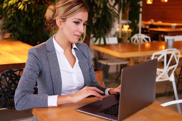 Trabajaba con una computadora portátil en la cafetería. Joven hermosa chica sentada en una cafetería y trabajando en la computadora . — Foto de Stock