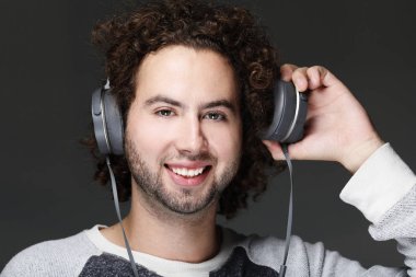 Kulaklık müzik dinlemek gülümseyerek mutlu bir genç adam. Gri arka plan üzerinde.