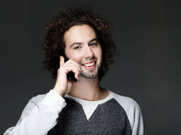 Sonriente joven hablando por teléfono inteligente y mirando a la cámara — Foto de Stock