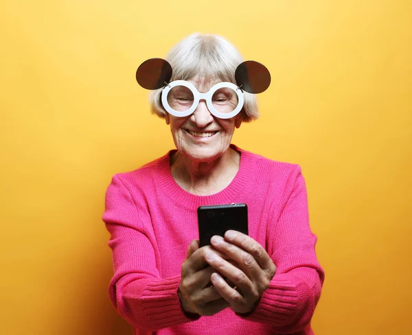 Stara babcia rozmawia przez telefon ze swoimi wnukami, uśmiecha się i wita je. — Zdjęcie stockowe