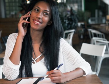 Yapılacaklar listesi yazmak ve getting haber Smartphone'da neşeli afro Amerikan hippi kız. Gülümseyen öğrenci ödev iyi haber üstünde hareket eden telefon ile bildirim okurken