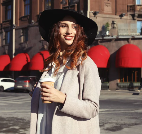 Souriant élégant jeune femme boire du café tout en marchant dans une rue de la ville — Photo