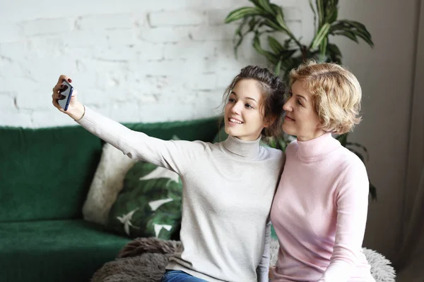 Beautiful mature mother and her daughter making a selfie using smart phone and smiling, home and happy. Lifestyle. — Stock Photo, Image