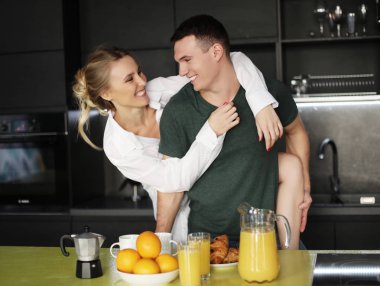 Güzel genç bir çift ayakta ve evde bir mutfakta sarılıyorlar.