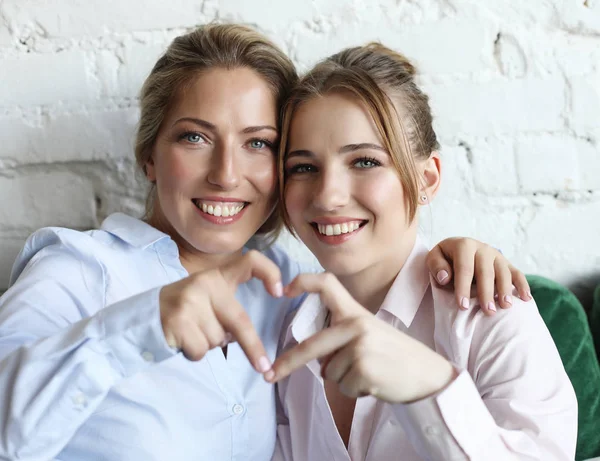 Madre e figlia amano. Donna adulta e giovane donna accatastamento mani nel segno del cuore guardando la fotocamera . — Foto Stock