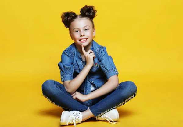 Το χαριτωμένο μικρό κορίτσι συνεδρίαση και χαμογελώντας, απομονωμένες σε κίτρινο φόντο — Φωτογραφία Αρχείου