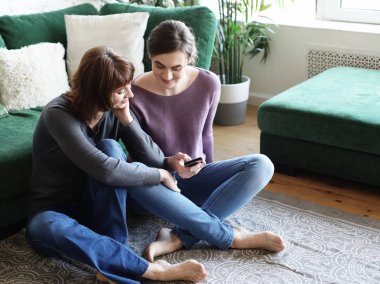  Evde akıllı telefon kullanan yaşlı bir kadın ve yetişkin kızı..