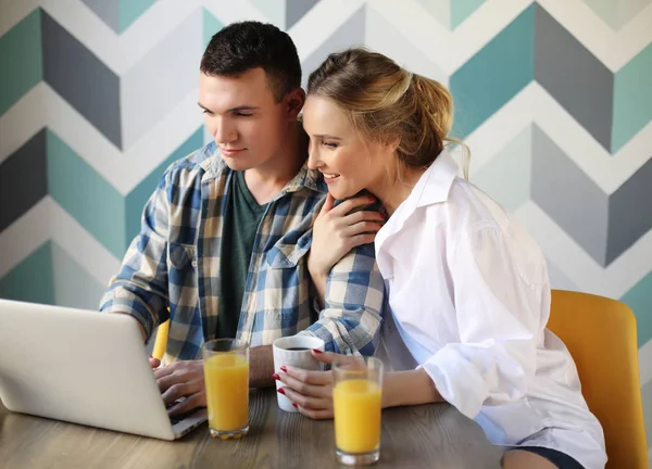 Loving couple having breakfast while sitting at the table in a kitchen at home and looking at laptop computer — Stock Photo, Image