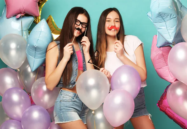 Ready for party. Two girls in stylish summer outfit , paper glasses and air balloons having fun and celebrate birthday.