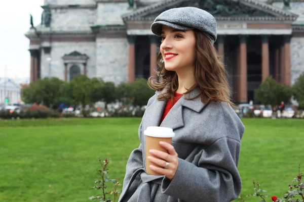 Χαμογελώντας κομψό νεαρή γυναίκα πίνοντας καφέ, ενώ το περπάτημα σε ένα δρόμο της πόλης — Φωτογραφία Αρχείου