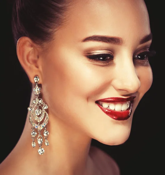 Beautiful brunette woman with bright make-up and jewelry earrings smiling close-up. Red lips and nails, evening make-up, luxurious look. — Stock Photo, Image