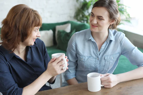 Beautiful mature mother and her adult daughter are drinking coffee — Stock Photo, Image