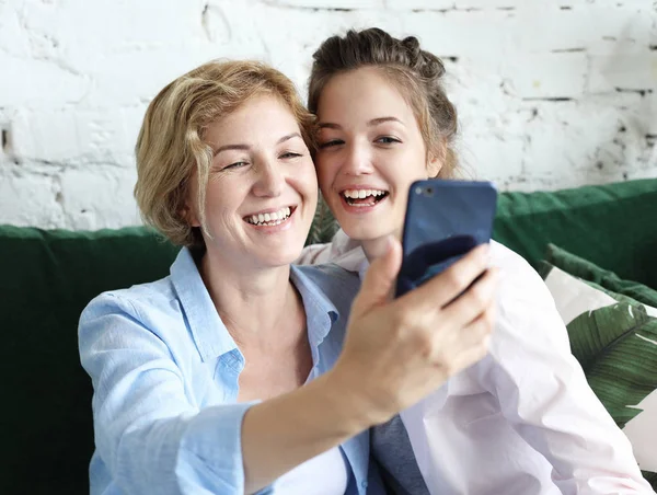 Портрет красивої зрілої матері і її дочки, що робить селфі за допомогою смартфона і посміхається, додому і щасливий . — стокове фото