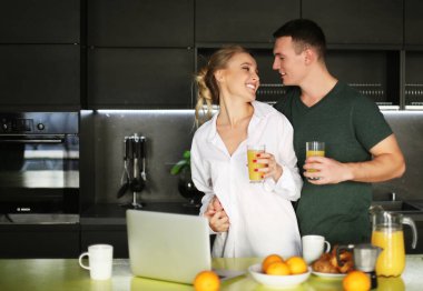 Genç çift mutfakta kahve içip dizüstü bilgisayarda çalışıyor.