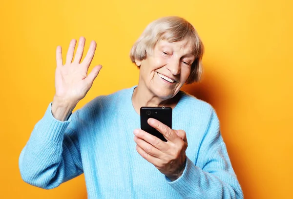 Gamla mormor pratar med sina barnbarn via telefon, ler och hälsar på dem. — Stockfoto