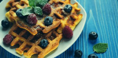 Taze sapılmak ve beyaz tabak, mavi ahşap zemin üzerine pudra şekeri ile geleneksel Belçika Waffle.
