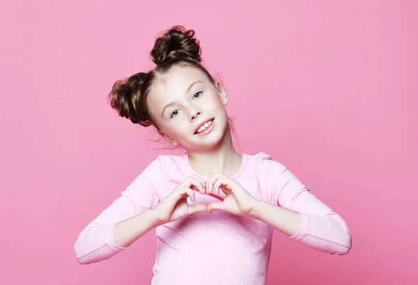 Bella ragazza bambino su sfondo rosa sorridente in amore che mostra il simbolo del cuore e la forma con le mani . — Foto Stock