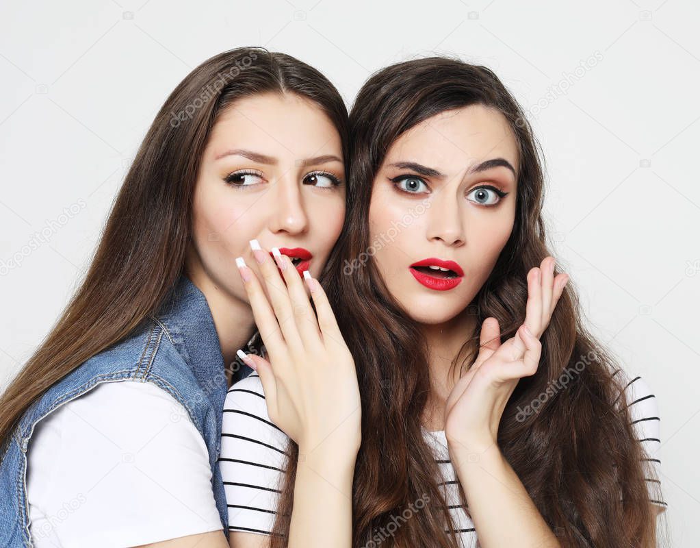 Portrait of two happy young women sharing secrets isolated over white  background