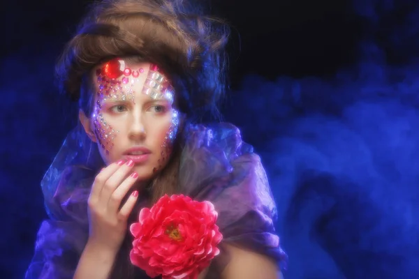 Jeune femme avec maquillage créatif tenant des fleurs — Photo