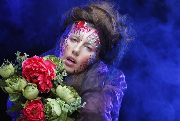 Mujer joven con maquillaje creativo sosteniendo flores — Foto de Stock