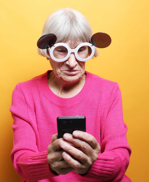 бабушка носит розовый свитер и большие солнечные очки на желтом фоне.