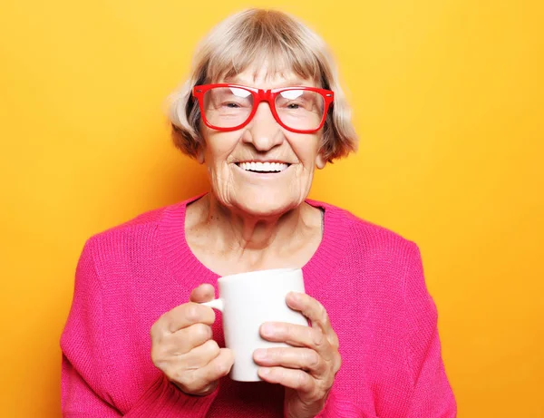 Portret starszej podekscytowanej pani uśmiechającej się, trzymającej filiżankę kawy, herbaty, napoju na żółtym tle — Zdjęcie stockowe