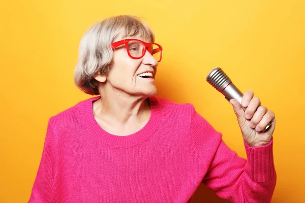 Estilo de vida y el concepto de la gente: Retrato de la abuela divertida sostiene el soporte del micrófono y canta aislado sobre fondo amarillo vivo — Foto de Stock