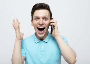 Cep telefonuyla konuşurken jest yapan ve gülümseyen tişörtlü genç adam.