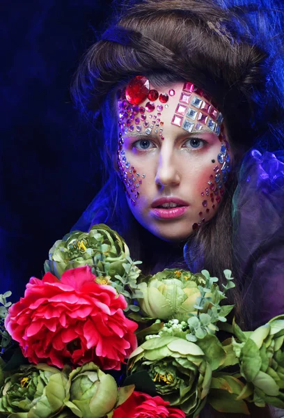 Junge Frau mit kreativem Make-up hält Blumen in der Hand — Stockfoto