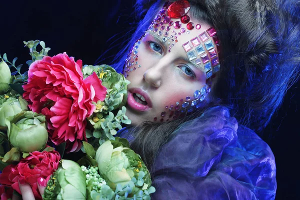 Junge Frau mit kreativem Make-up hält Blumen in der Hand — Stockfoto