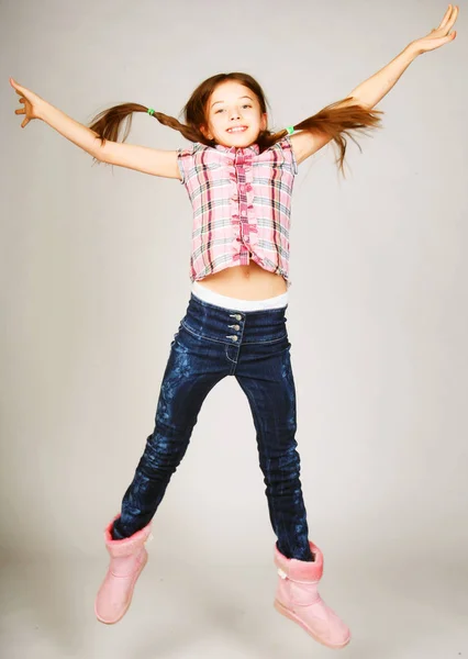 Μικρό ξανθό κορίτσι άλματα σε ένα γκρίζο φόντο — Φωτογραφία Αρχείου