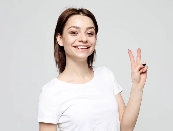 Šťastná dívka dívá na fotoaparát s úsměvem a ukazující mír znamení s prsty — Stock fotografie