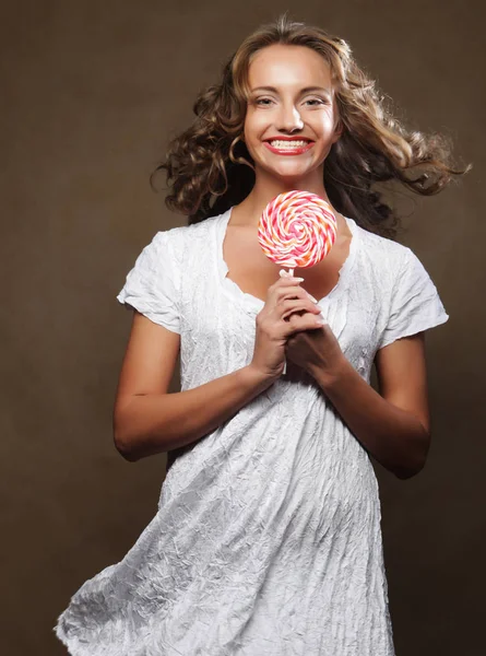 Beautiful young curly girl holding a red white lollipop and smiling. — Stock Photo, Image
