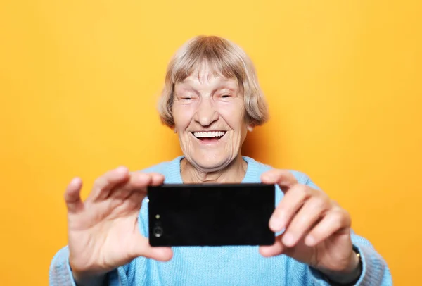 Стиль жизни, технологии и концепция людей: бабушка улыбается и делает селфи на жёлтом фоне — стоковое фото