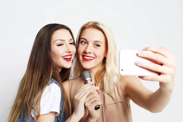 Dos chicas de belleza con un micrófono tomar selfie con teléfono inteligente —  Fotos de Stock