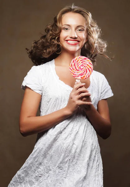 Beautiful young curly girl holding a red white lollipop and smiling. — Stock Photo, Image