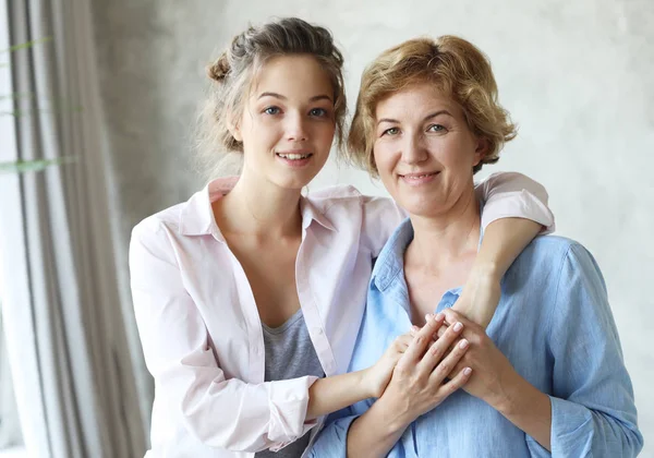 Beautiful senior mom and her adult daughter are hugging, looking at camera and smiling