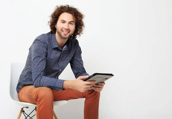 Homem casual feliz em uma cadeira com um tablet pc, isolado no fundo branco — Fotografia de Stock