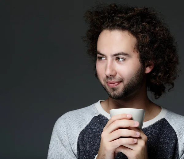 Перерва на каву. Красивий молодий чоловік тримає чашку кави і посміхається, стоячи на сірому фоні . — стокове фото