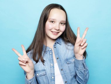 Mutlu kız gülümseyerek kameraya bakıyor ve barış işaretini parmaklarıyla gösteriyor.