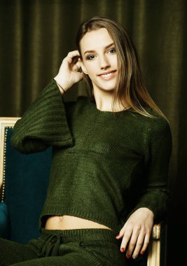 Onun tarzı rahat hissediyor. Büyük bir rahat sandalyede oturuyor ve kameraya bakarak gündelik kıyafeti giymiş güzel ve genç birbayan stüdyo çekim