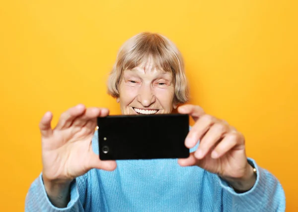 Livsstil, tehnologi och människor koncept: mormor ler och tar en selfie över gul bakgrund — Stockfoto