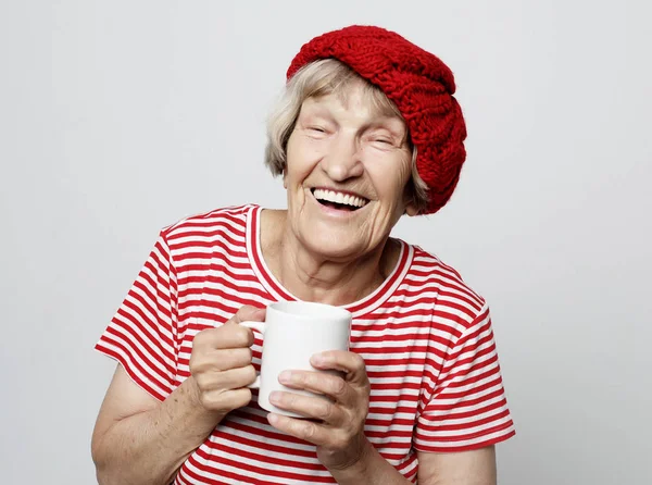 Gülümseyen, elinde fincanla kahve ya da çay içen heyecanlı yaşlı kadın. — Stok fotoğraf