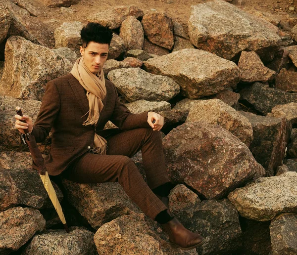 Jovem elegante sentado nas rochas perto do mar — Fotografia de Stock