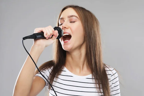 Güzellik modeli kız şarkıcı ışık gri arka plan üzerinde bir mikrofon ile — Stok fotoğraf